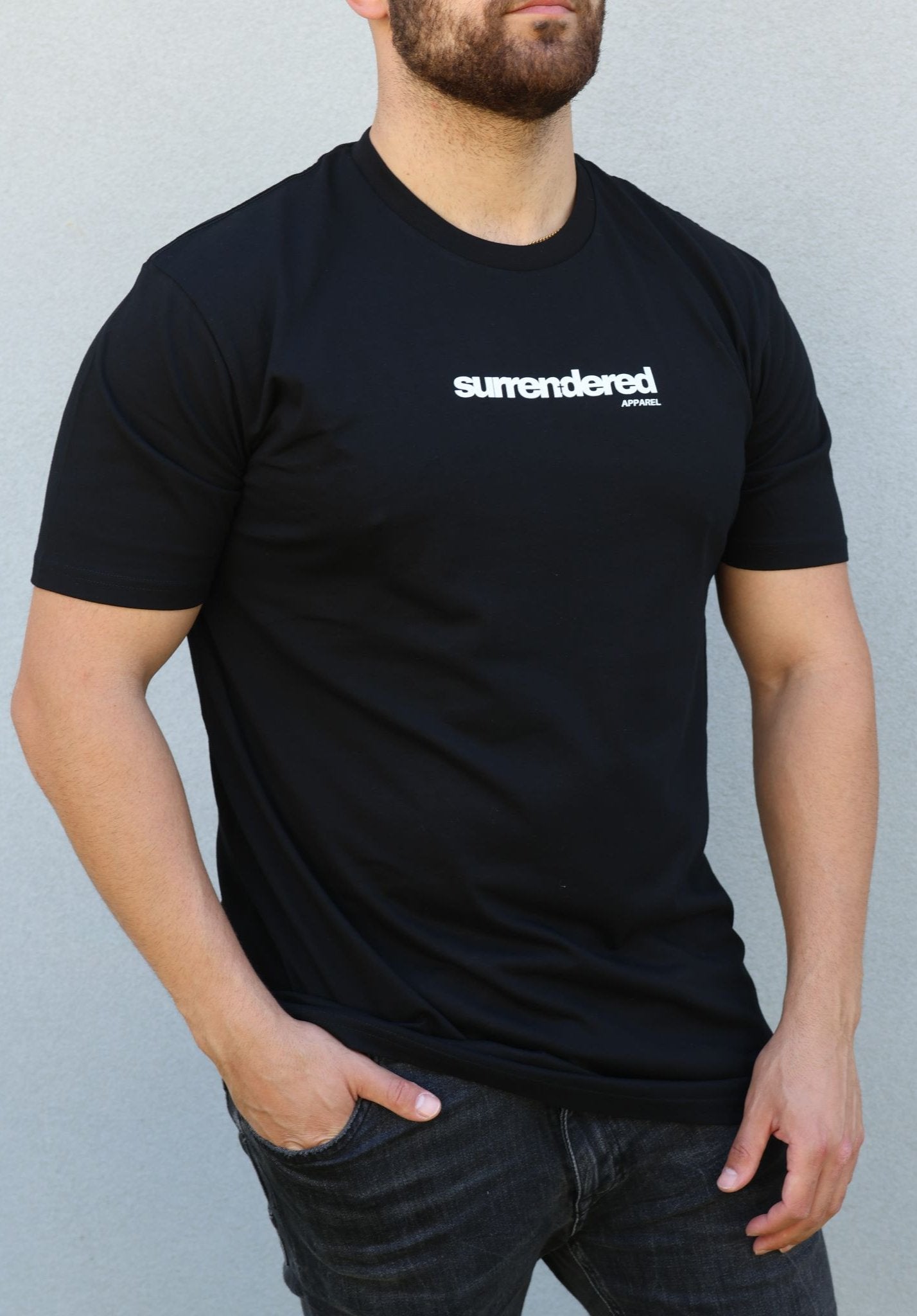 Man wearing the Surrendered Apparel Essential Crew Neck T-shirt in Black. Light Cotton shirt in black, white Surrendered Apparel logo across the front of the chest. Man is wearing black Jeans